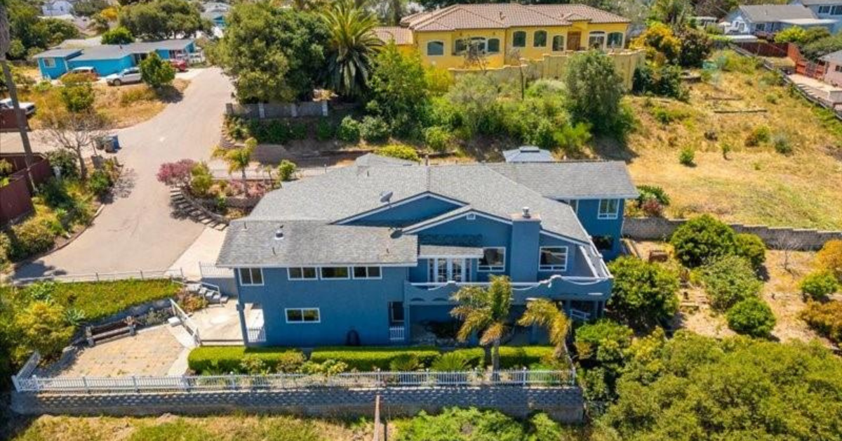 Aerial view of 1039 Ritchie Road, one of the recently sold homes by The Nichols Real Estate Team, showing a large two story blue residence with landscaped terraced yard and hillside surroundings.