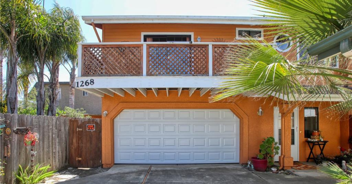Front exterior of the home at 1268 Baden Avenue, featuring a bright orange stucco finish, large balcony with lattice railing, a white two car garage, and tropical landscaping.