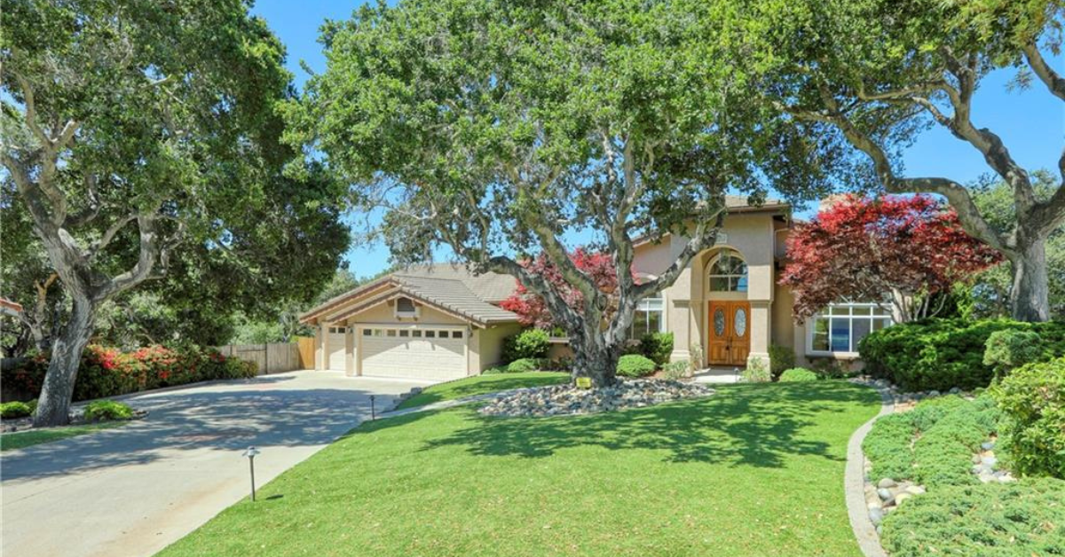 Front exterior of the home on Vista Circle, featuring a well maintained lawn, mature trees, vibrant landscaping, and a two story residence with a three car garage.